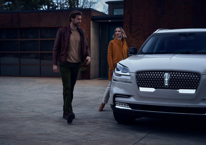 A man and a woman approaching a 2024 Lincoln Aviator® SUV, which illuminates certain lights when they are close | Doggett Lincoln of Beaumont in Beaumont TX