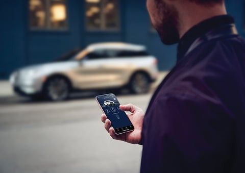 A person is shown interacting with a smartphone to connect to a Lincoln vehicle across the street. | Doggett Lincoln of Beaumont in Beaumont TX
